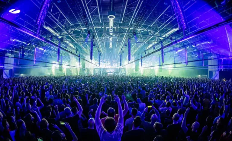 La foule rassemblée dans la grande salle de l’Ahoy Rotterdam lors d’un événement A State Of Trance, sous un vaste dispositif de lumières bleues et d’écrans.