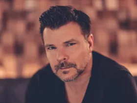 Portrait d’ATB, regard face caméra, dans une ambiance chaleureuse et intimiste, sur fond flou aux teintes brunes.