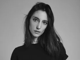 Portrait en noir et blanc d'Amelie Lens, DJ et productrice belge, avec un regard intense et des cheveux mi-longs, vêtue d'un haut noir sur fond neutre.
