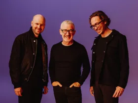 Above & Beyond posant ensemble sur fond violet, tous trois habillés en noir et souriants, lors de la promotion de l’album Bigger Than All Of Us.