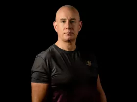 Mark Sherry en portrait studio, vêtu d'un t-shirt noir et rouge dégradé, sur fond noir.