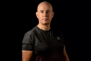 Mark Sherry en portrait studio, vêtu d'un t-shirt noir et rouge dégradé, sur fond noir.