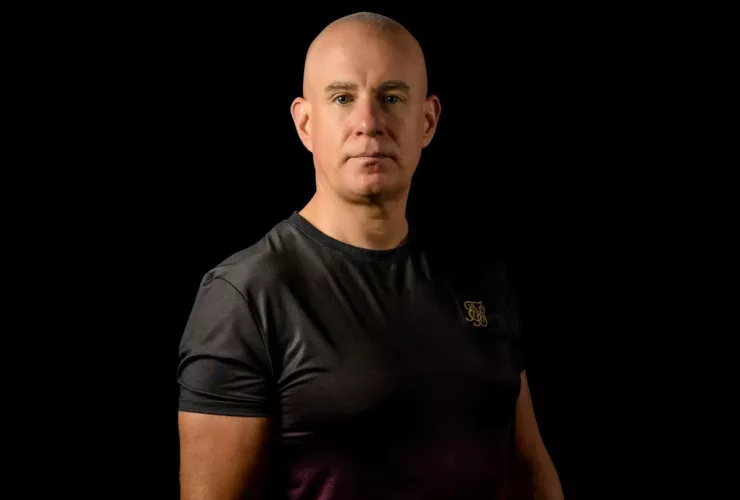 Mark Sherry en portrait studio, vêtu d'un t-shirt noir et rouge dégradé, sur fond noir.
