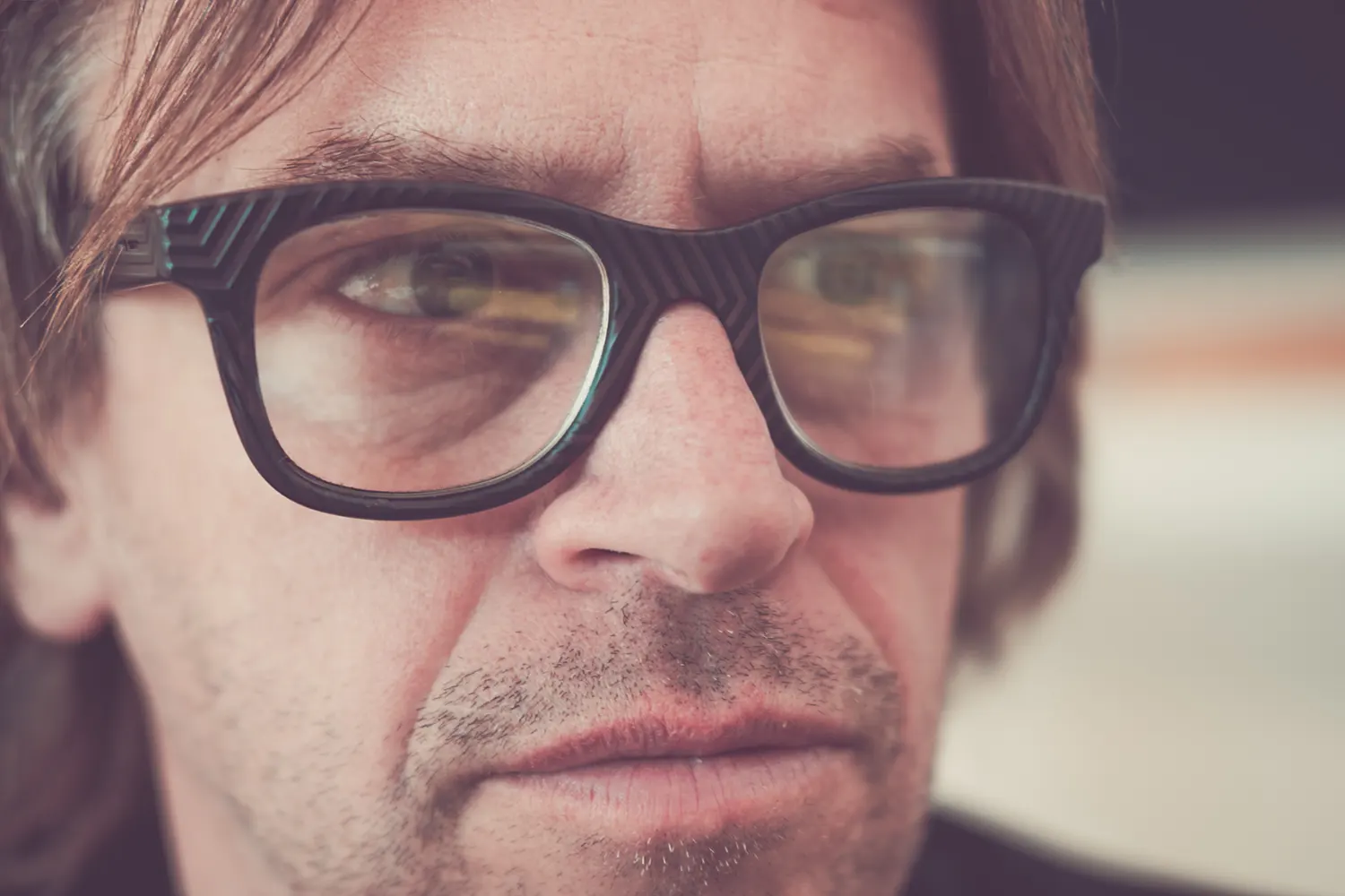 Portrait en gros plan de Chicane, portant des lunettes à monture noire et affichant un regard concentré.