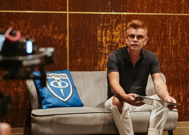 Paul Oakenfold assis sur un canapé orné d’un coussin au logo Perfecto Records, lors d’une interview célébrant les 35 ans du label.