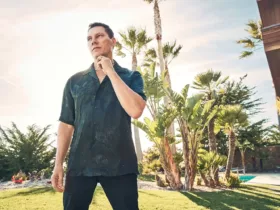 Portrait de Tiësto en extérieur, dans une ambiance ensoleillée et détendue, entouré de palmiers et de verdure.