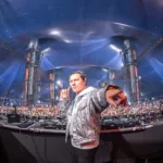 Tiësto sur scène lors d’un DJ set à grande échelle, devant une foule massive.