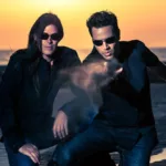 Le duo Astral Projection, figure emblématique de la Trance Goa, photographié sur une plage au coucher du soleil, dans une ambiance cinématique et mystique.