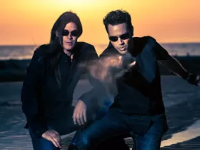 Le duo Astral Projection, figure emblématique de la Trance Goa, photographié sur une plage au coucher du soleil, dans une ambiance cinématique et mystique.