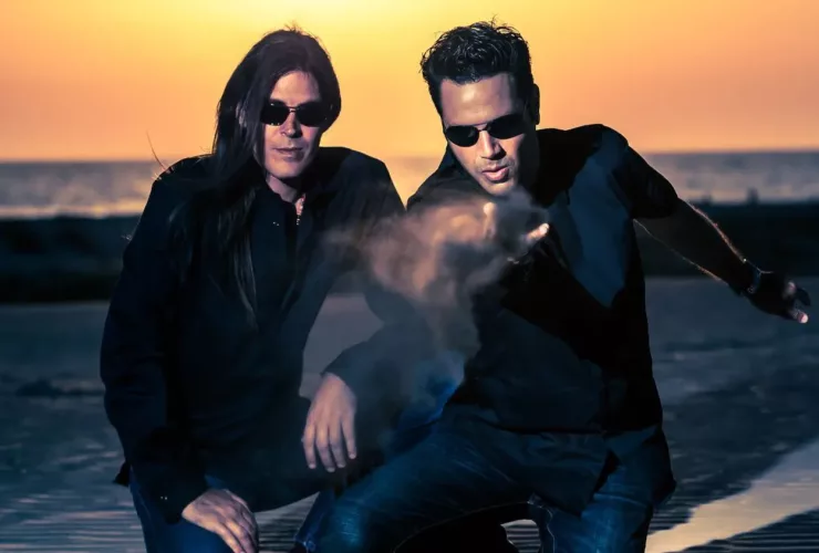 Le duo Astral Projection, figure emblématique de la Trance Goa, photographié sur une plage au coucher du soleil, dans une ambiance cinématique et mystique.