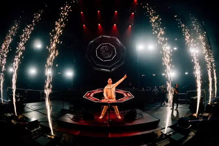 Giuseppe Ottaviani sur scène derrière son dispositif scénique OTTAGON, entouré d’effets pyrotechniques et de lumières rouges.