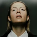 Portrait de Charlotte de Witte, regard tourné vers le haut, éclairée par une lumière contrastée sur fond sombre.