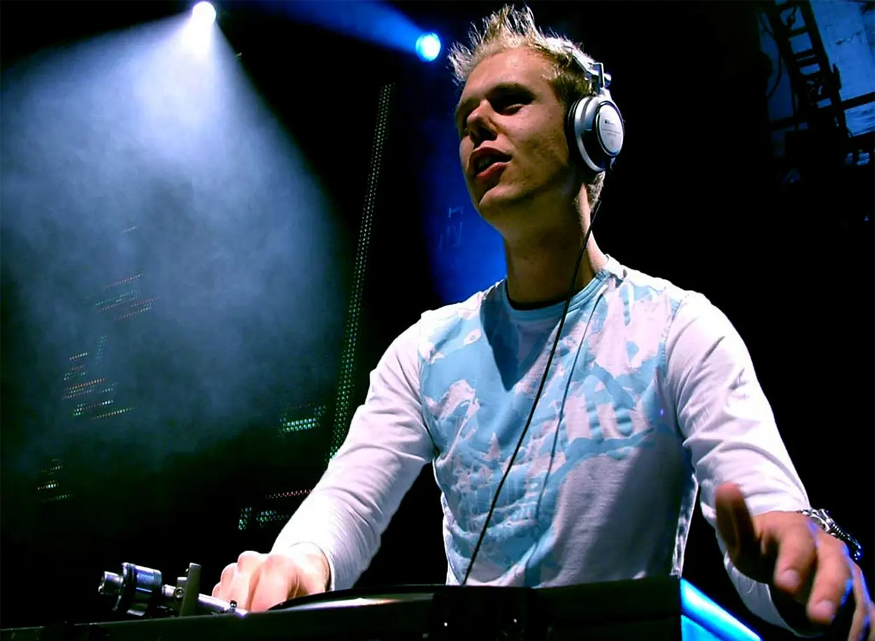 Armin van Buuren en DJ set au début des années 2000, concentré derrière ses platines sous une lumière bleue en club.