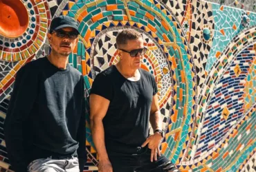 Le duo Cosmic Gate photographié devant une fresque en mosaïque colorée, dans une ambiance ensoleillée.