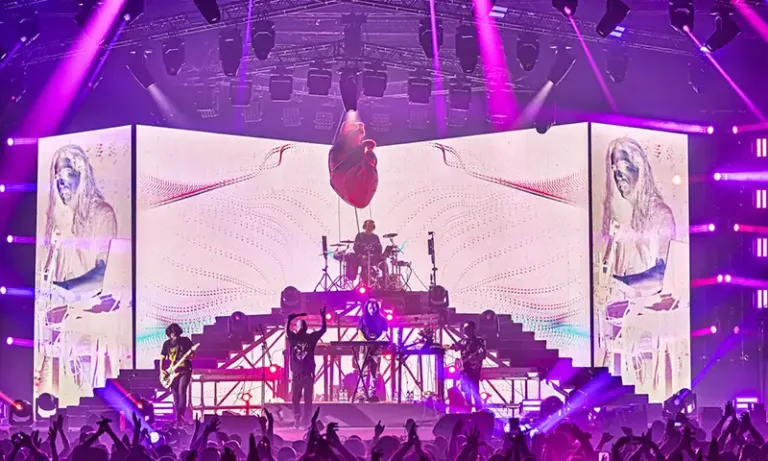 Infected Mushroom en concert à Expo Tel Aviv, avec un dispositif scénique imposant composé d’écrans géants, lumières violettes et visuels psychédéliques, devant un public en liesse.