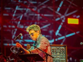 Jean-Michel Jarre en concert, manipulant ses instruments électroniques sur scène, sous un éclairage rouge et un décor lumineux.