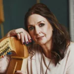 Moya Brennan posant avec une harpe, dans un environnement musical en studio.