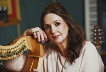Moya Brennan posant avec une harpe, dans un environnement musical en studio.
