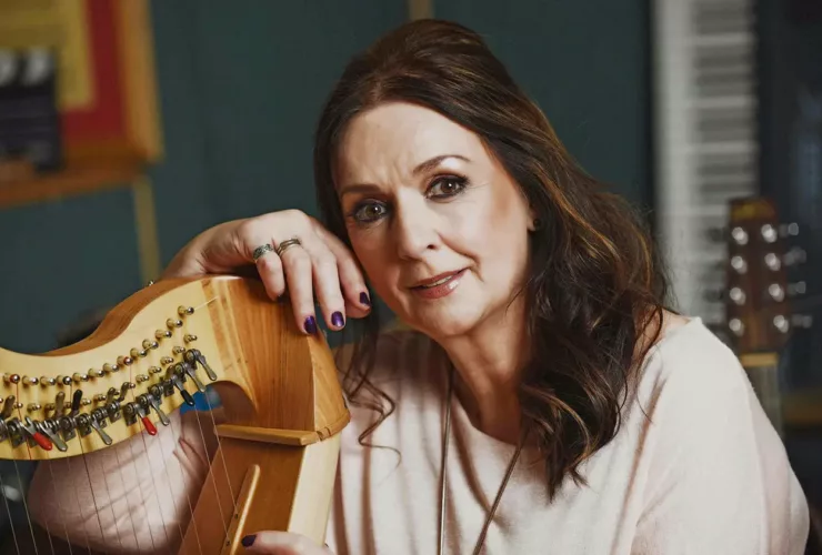 Moya Brennan posant avec une harpe, dans un environnement musical en studio.