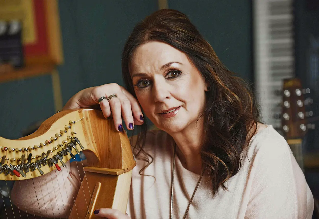 Moya Brennan posant avec une harpe, dans un environnement musical en studio.