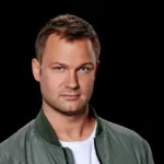 Portrait de Jeffrey Sutorius sur fond noir, portant une veste verte et un t-shirt blanc, regard tourné vers l’objectif.