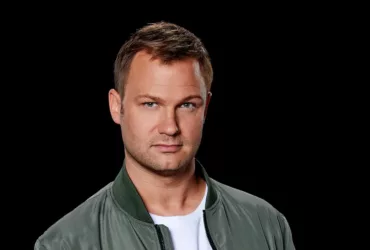 Portrait de Jeffrey Sutorius sur fond noir, portant une veste verte et un t-shirt blanc, regard tourné vers l’objectif.
