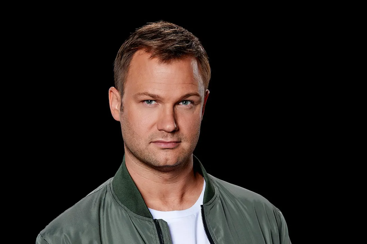 Portrait de Jeffrey Sutorius sur fond noir, portant une veste verte et un t-shirt blanc, regard tourné vers l’objectif.
