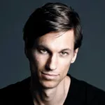 Portrait de Menno de Jong sur fond sombre, vêtu d’un t-shirt noir, regard fixé vers l’objectif avec une expression calme et déterminée.