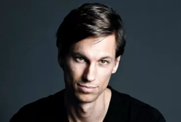 Portrait de Menno de Jong sur fond sombre, vêtu d’un t-shirt noir, regard fixé vers l’objectif avec une expression calme et déterminée.