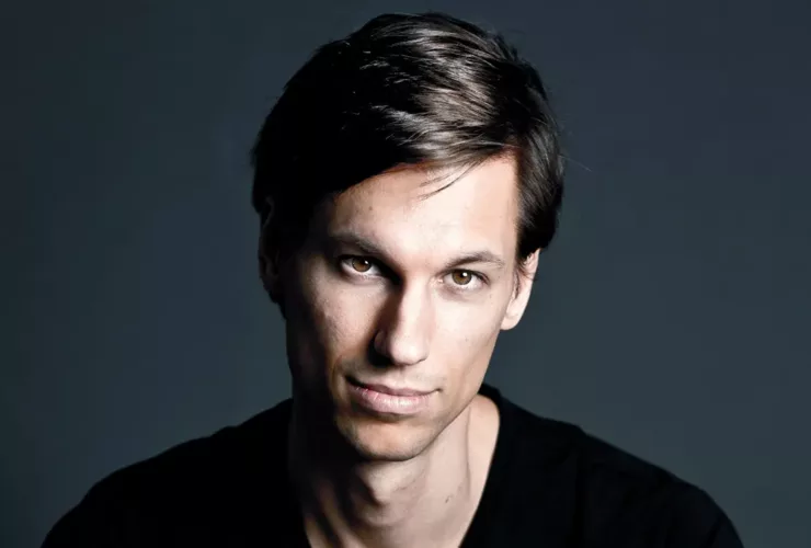 Portrait de Menno de Jong sur fond sombre, vêtu d’un t-shirt noir, regard fixé vers l’objectif avec une expression calme et déterminée.