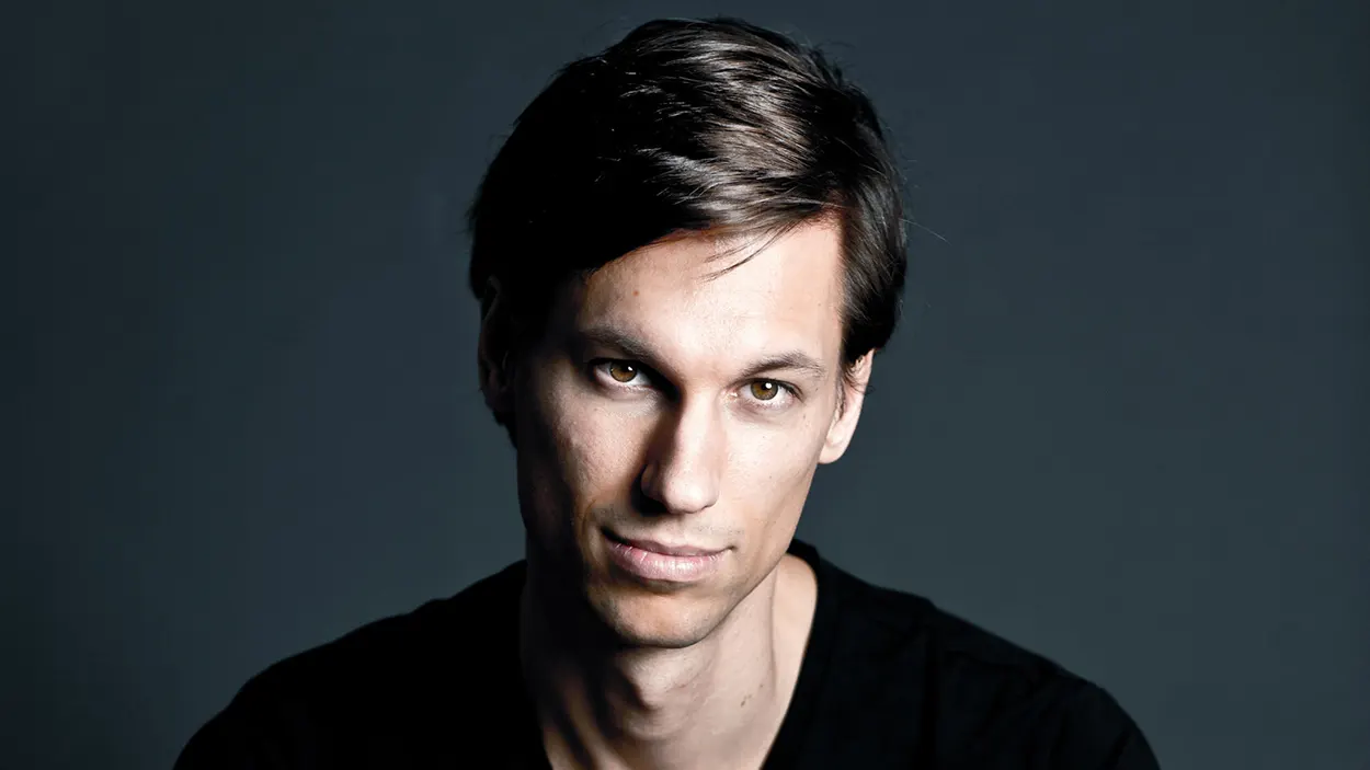 Portrait de Menno de Jong sur fond sombre, vêtu d’un t-shirt noir, regard fixé vers l’objectif avec une expression calme et déterminée.