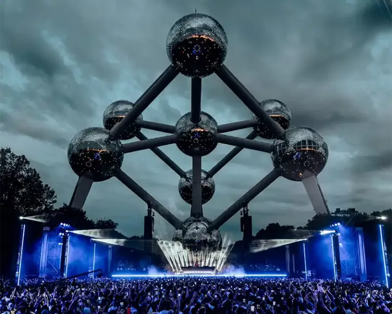 L’Atomium de Bruxelles domine la scène du concert de Tiësto, illuminée en bleu devant une foule immense sous un ciel nuageux.