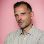 Portrait de Benno de Goeij, membre de Rank 1 et producteur derrière le projet Trance The Quest, posant devant un fond rose.