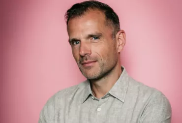 Portrait de Benno de Goeij, membre de Rank 1 et producteur derrière le projet Trance The Quest, posant devant un fond rose.