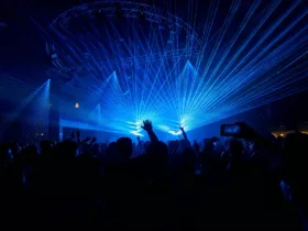 Foule lors d’une soirée de musique électronique, les bras levés sous un impressionnant jeu de lasers bleus.