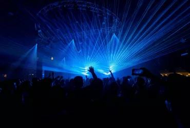 Foule lors d’une soirée de musique électronique, les bras levés sous un impressionnant jeu de lasers bleus.