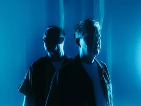 Sasha et John Digweed posent dans une lumière bleue intense, photographiés de trois quarts dans une ambiance sombre et atmosphérique pour “Northern Exposure Redux”.