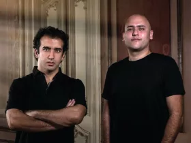 Aly & Fila posent côte à côte, vêtus de noir, devant des boiseries aux moulures classiques