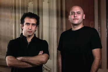 Aly & Fila posent côte à côte, vêtus de noir, devant des boiseries aux moulures classiques