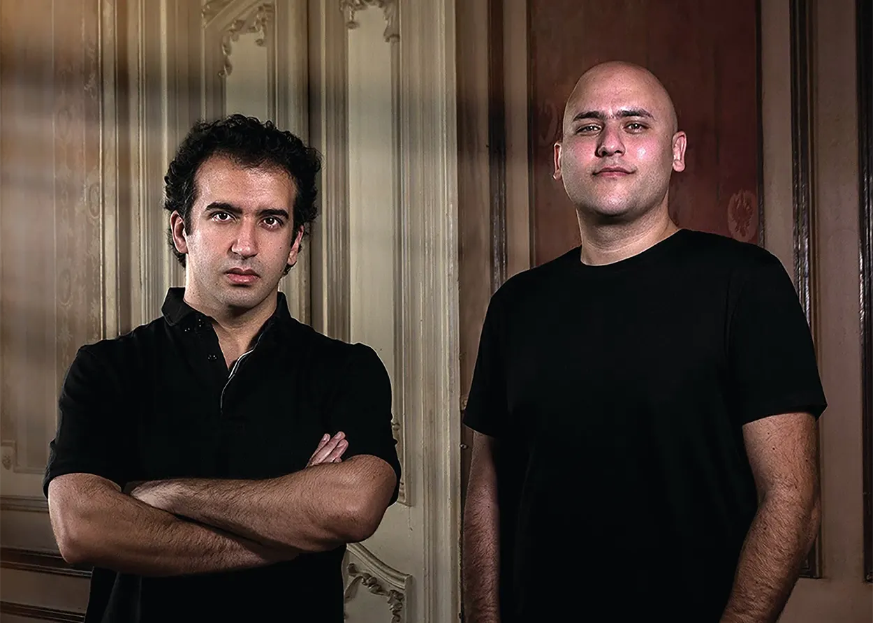 Aly & Fila posent côte à côte, vêtus de noir, devant des boiseries aux moulures classiques